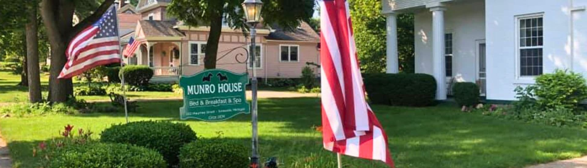 A sign for the Munro House Bed & Breakfast, flanked by American flags and surrounded by a lush green lawn.