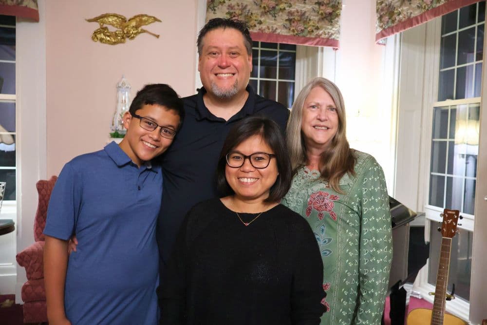 A family of four poses together indoors, smiling at the camera.