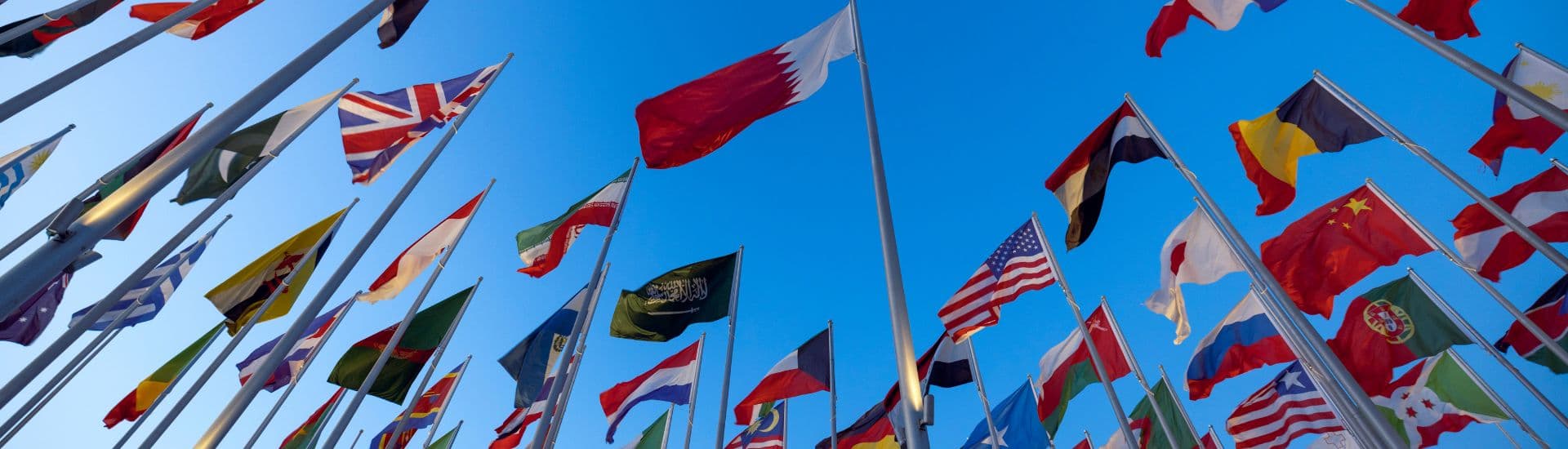 A cluster of various national flags waving against a clear blue sky.