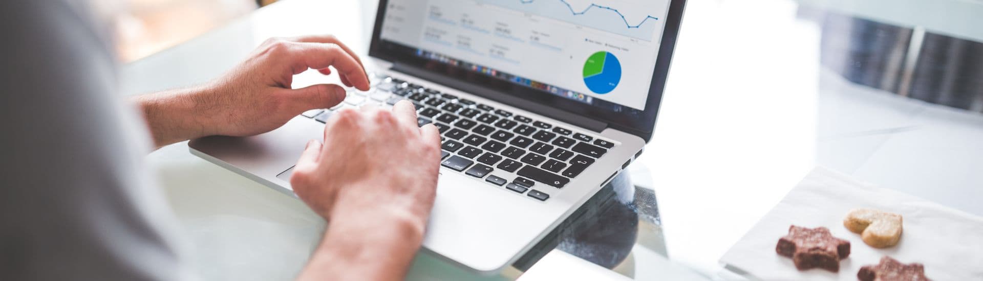 A person types on a laptop displaying data charts while sitting at a table with snacks.