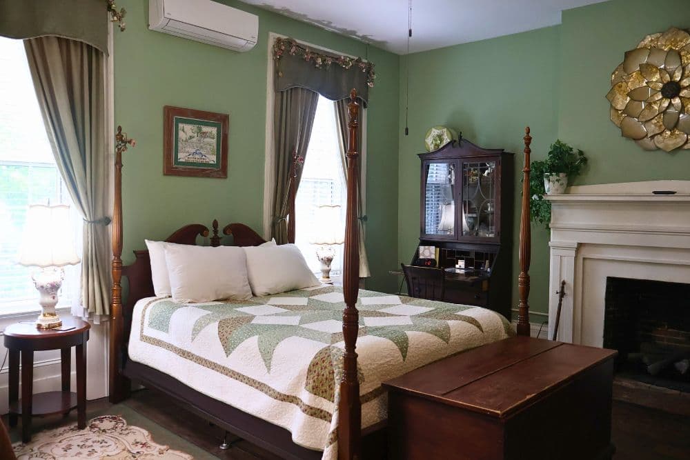 A cozy bedroom featuring a bed with a quilt, a wooden dresser, and green walls.