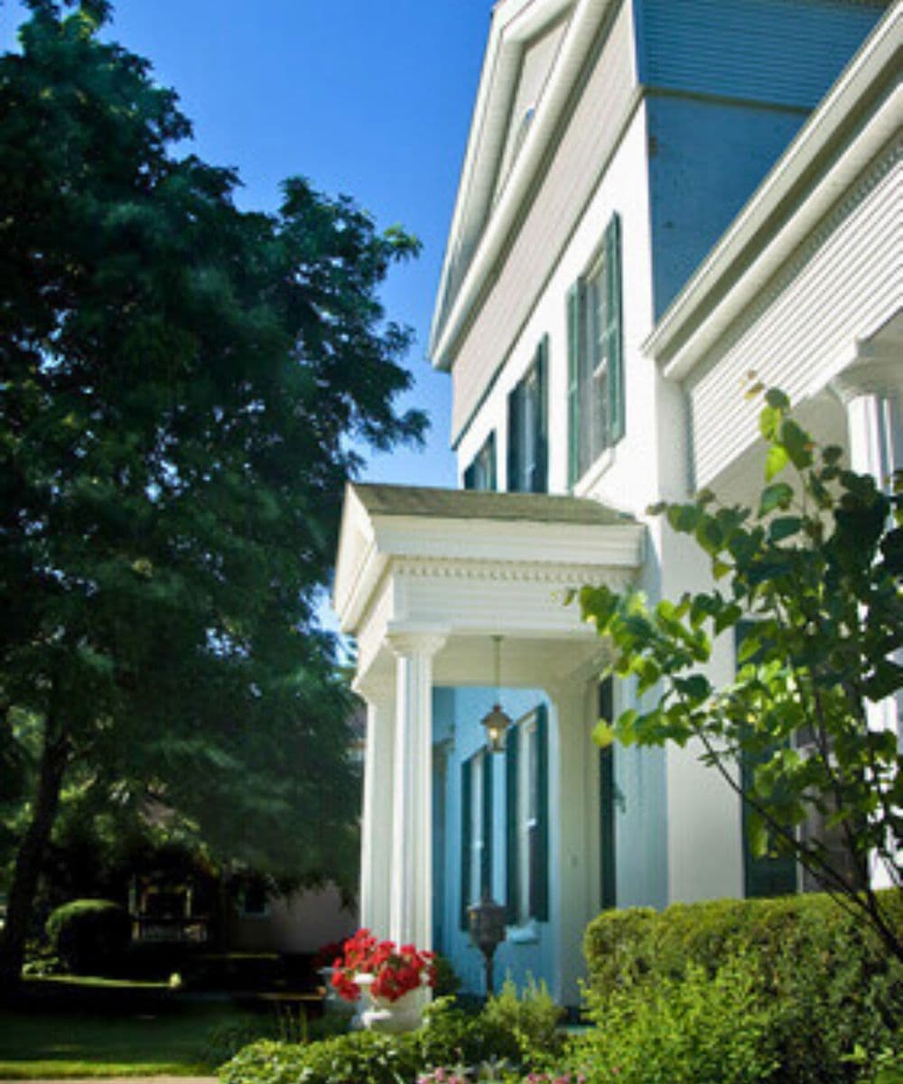 A charming white house with green shutters, featuring a covered porch and vibrant flowers.