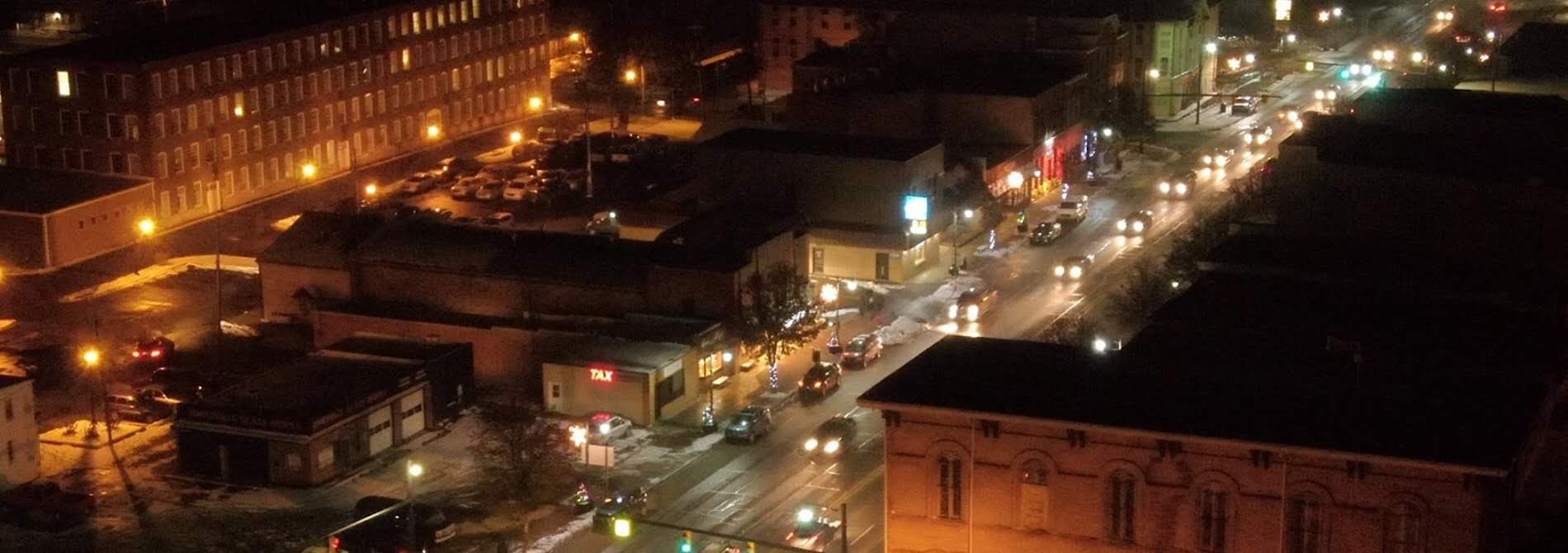Aerial view of a city street illuminated at night, with traffic and buildings visible.