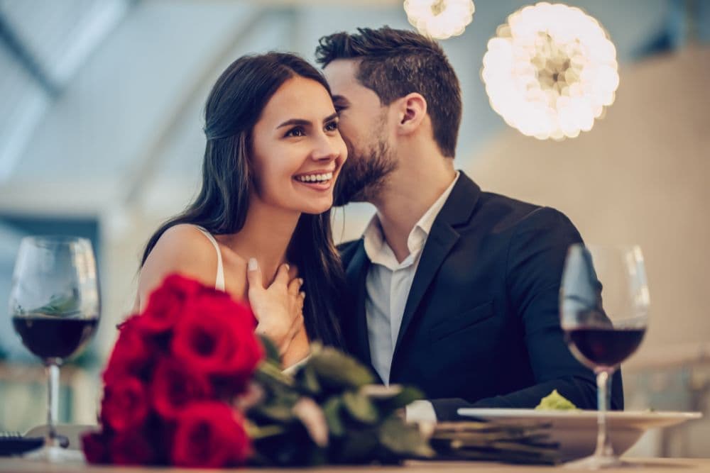 A couple enjoys a romantic dinner together, surrounded by roses and wine.
