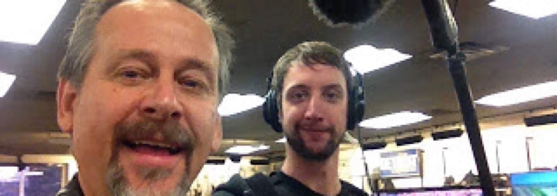 Two men smiling for a selfie in a recording studio, one holding a microphone. Two men smiling for a selfie in a recording studio, one holding a microphone.