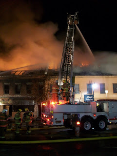 firefighter on ladder truck spraying burning building at night