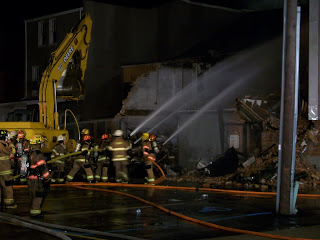 firefighters using hoses to douse smoldering building at night