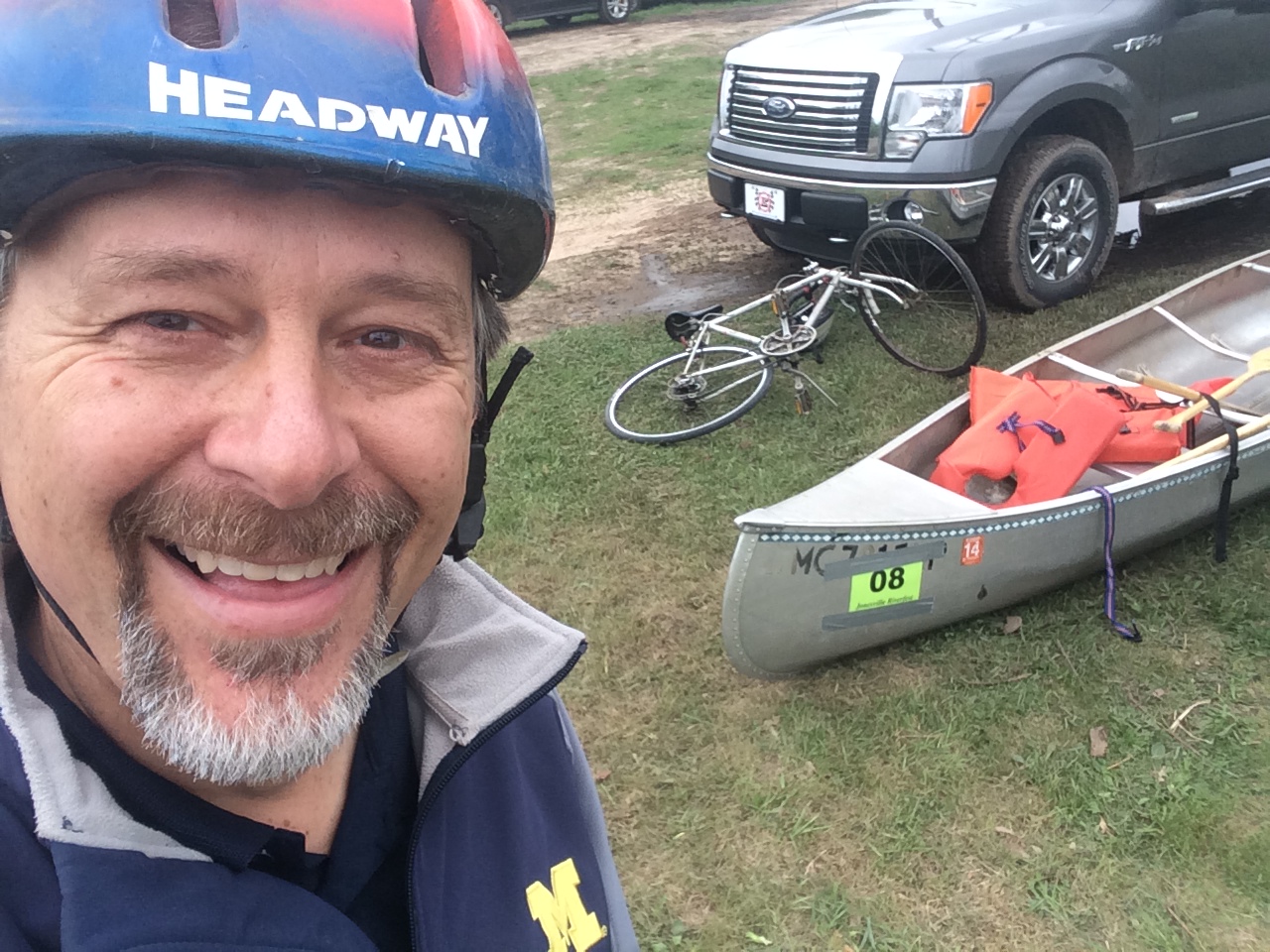 Smiling man wearing a blue bicyclist helmet with white bicycle and aluminum canoe with orange life preserver