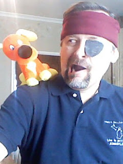 man with maroon headband and eye patch with an orange dog perched on his shoulder