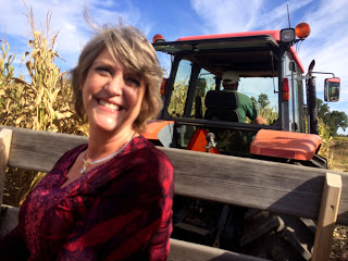 Smiling lady in red riding in a tractor pulled wagon through a corn field