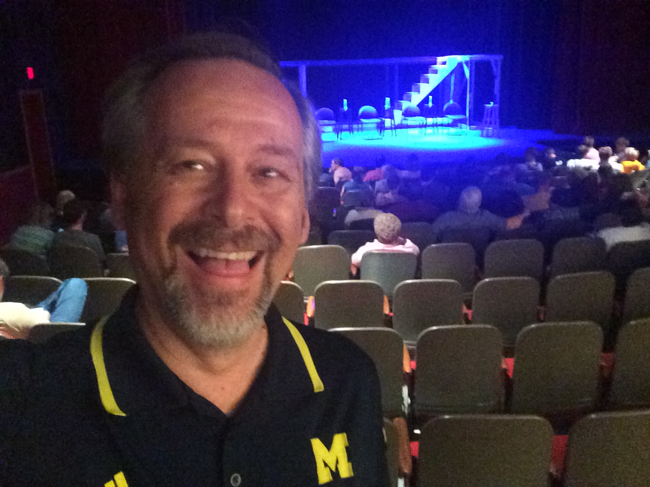 smiling man in theater with blue lit stage in background