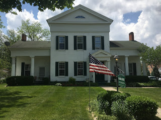 American flag flying outside white greek revival style home