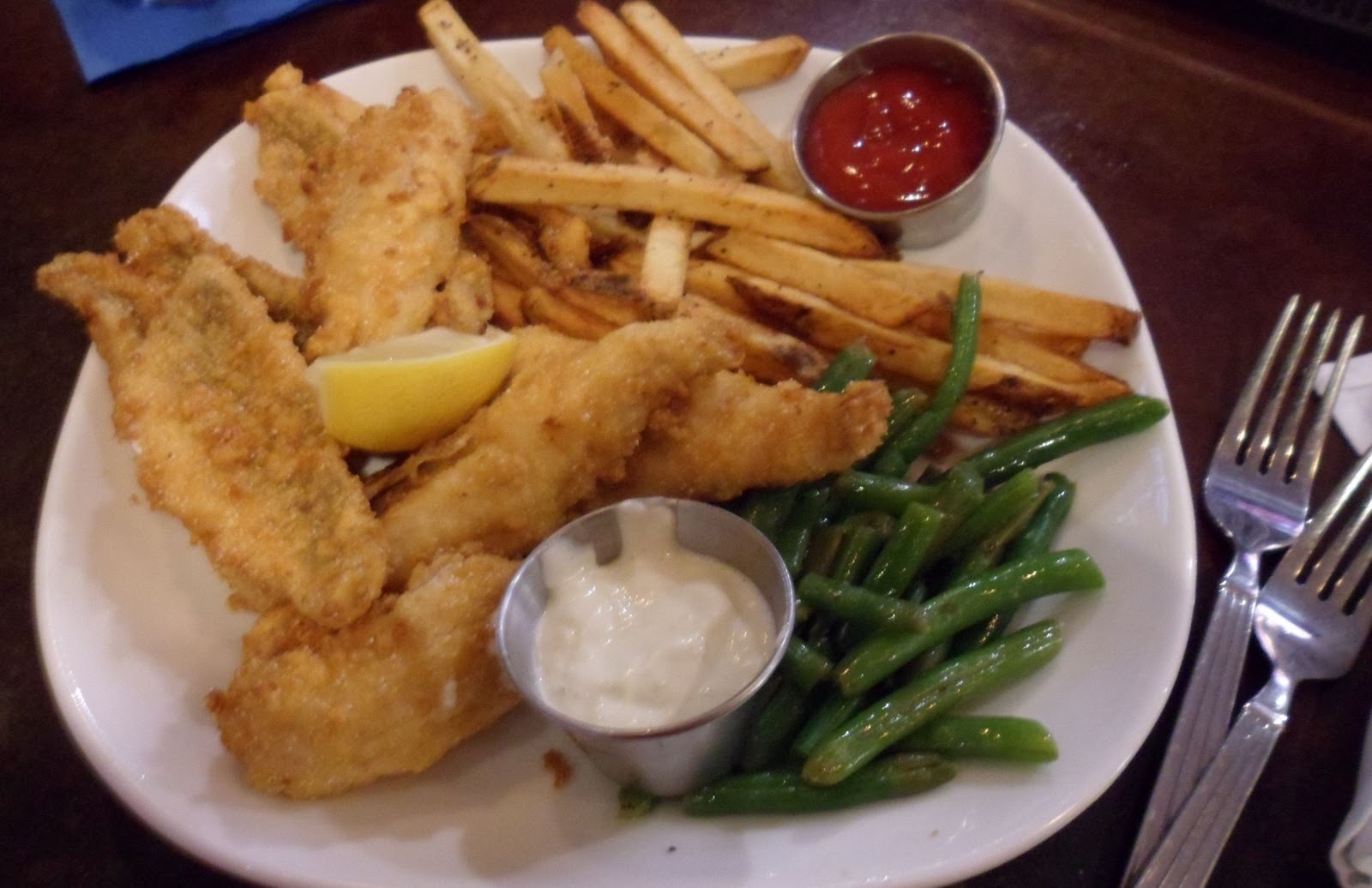 Fish dinner on a white plate including green beans and French fries