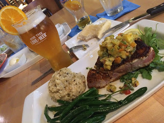 golden beer with an orange slice accompanies steak rice and green beans