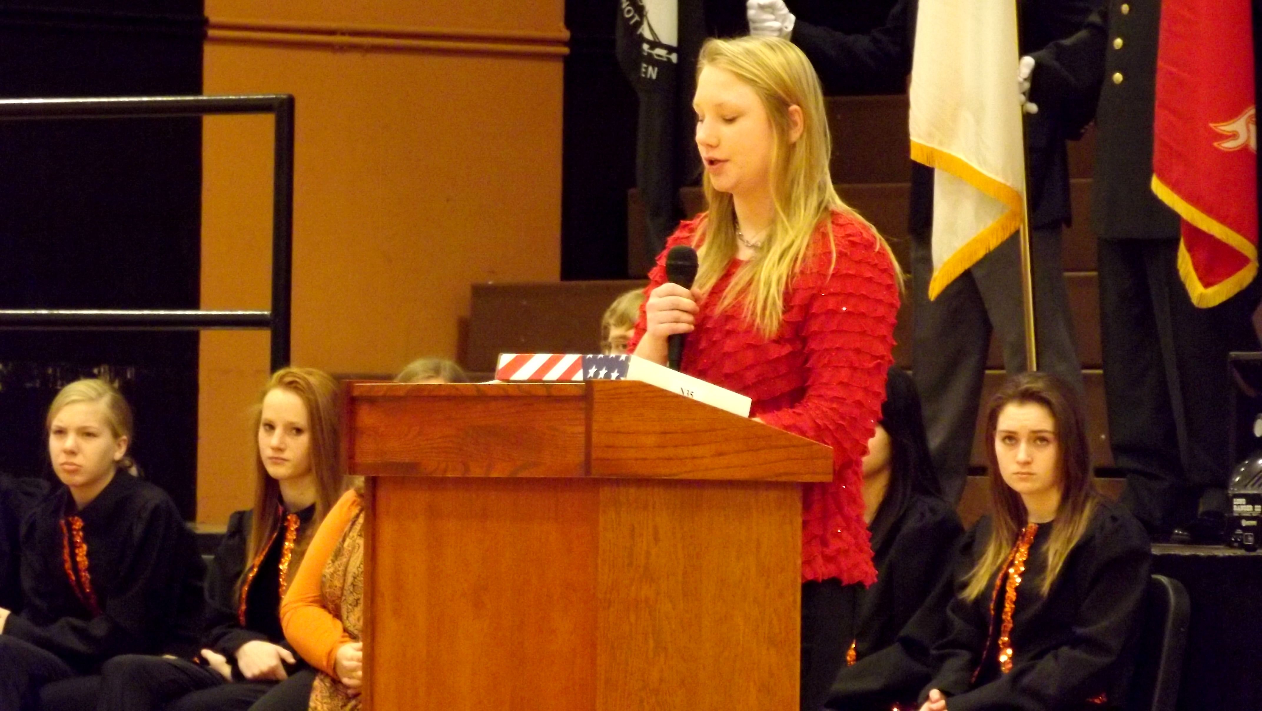 young woman in red sweater giving a speech at a podium
