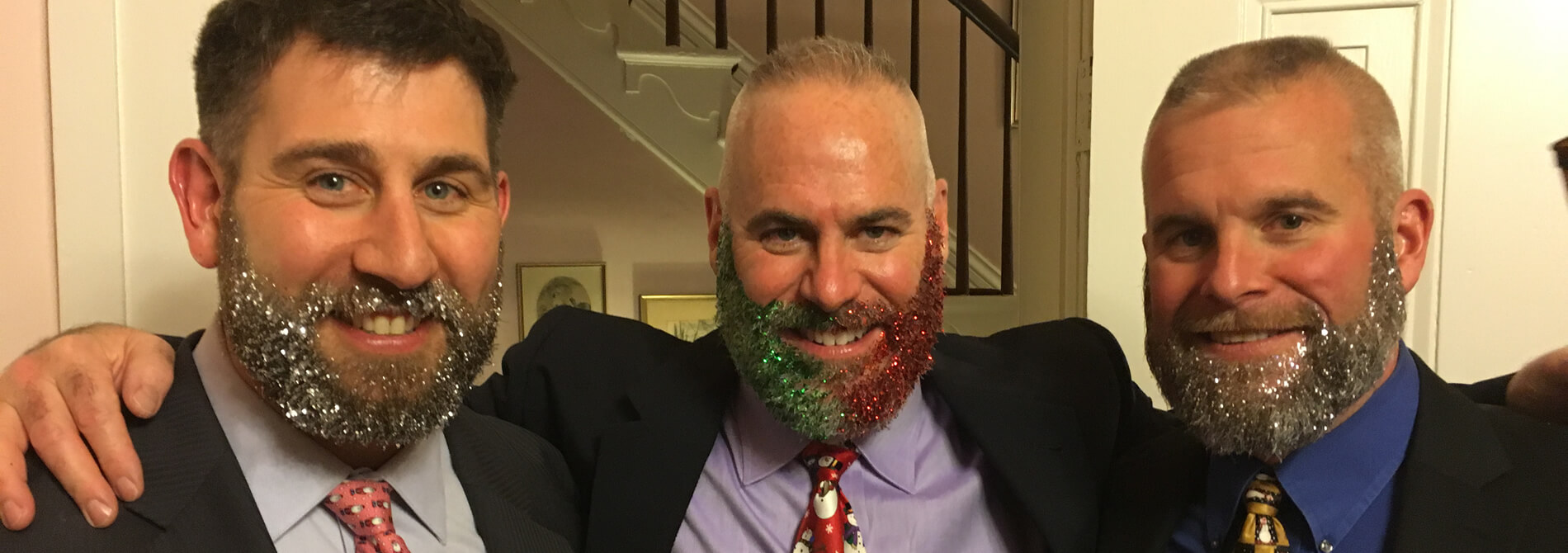 three businessmen wearing black suits and red or gold ties have silver red and green glitter beards