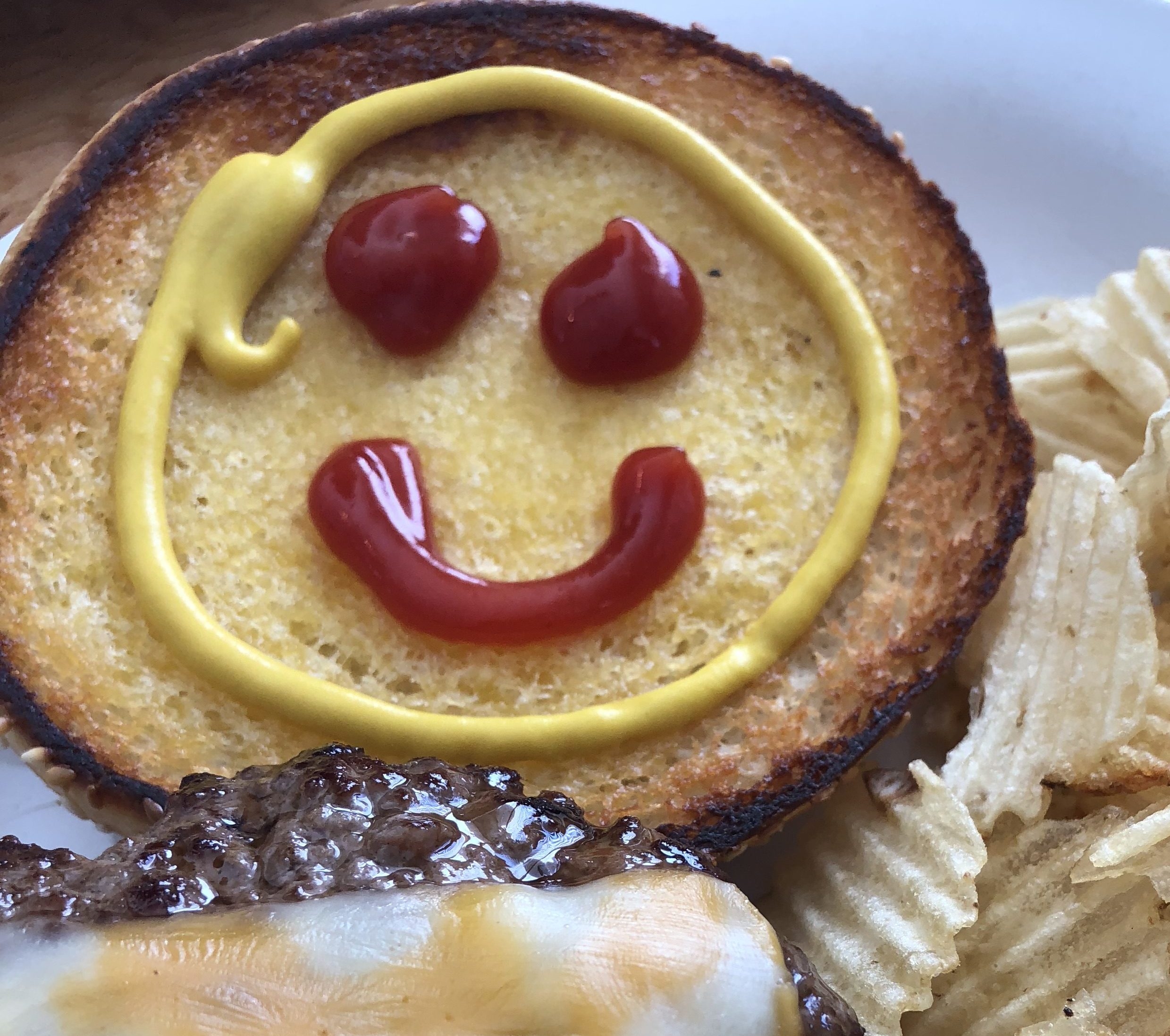 happy face drawn with ketchup and mustard on the toasted bun of a hamburger