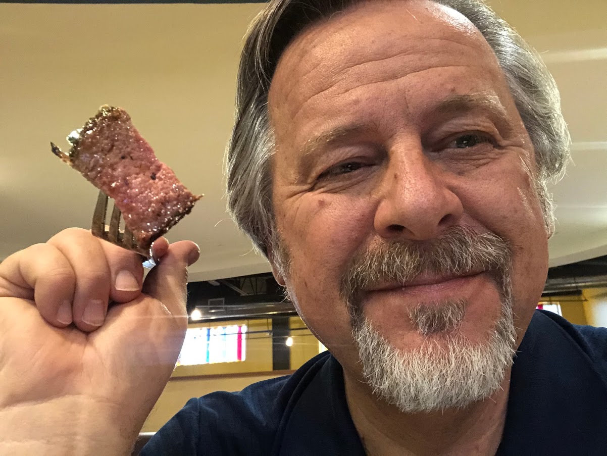 satisfied man holding a piece of steak on a fork
