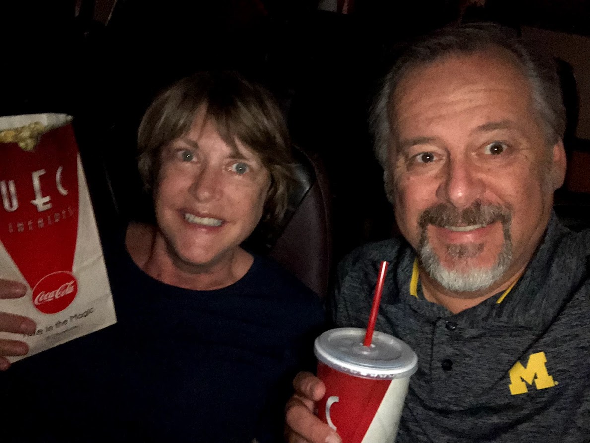 man and woman in a movie theater holding popcorn and beverage