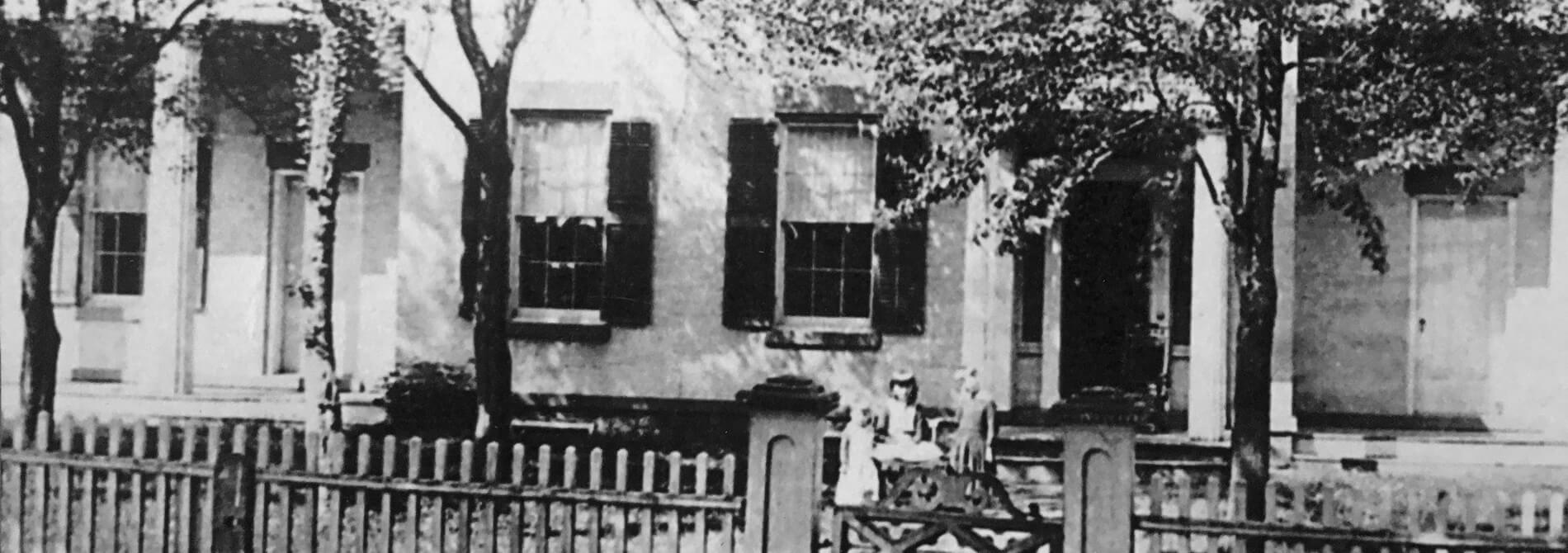 antique black and white photograph of munro house in the 1800s surrounded by a picket fence