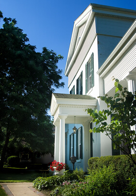 Acute angle view of white greek revival style munro house with green shrubbery